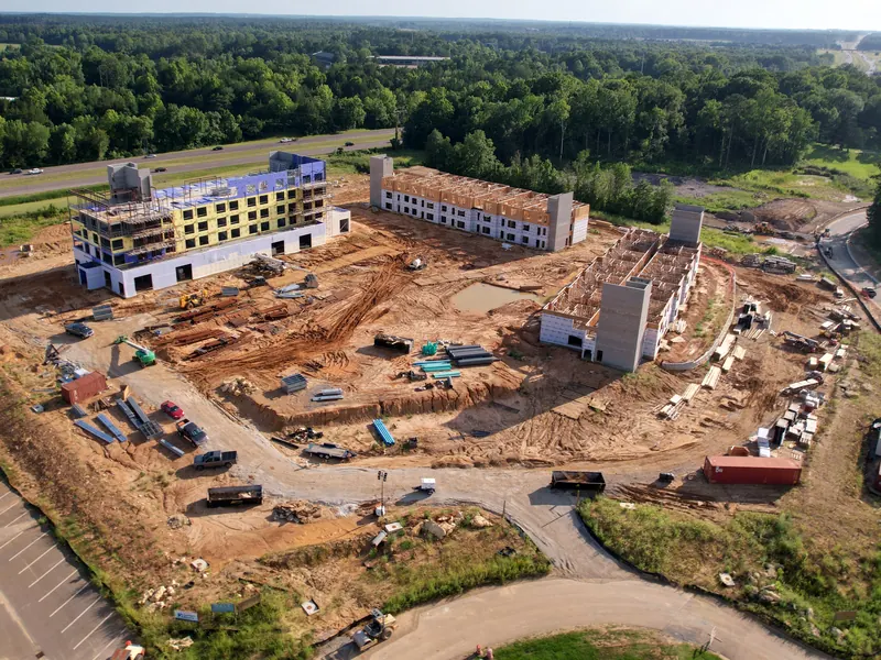 Angled drone photo of the same hotel build beside the highway, main building sheathed and two wings framed.