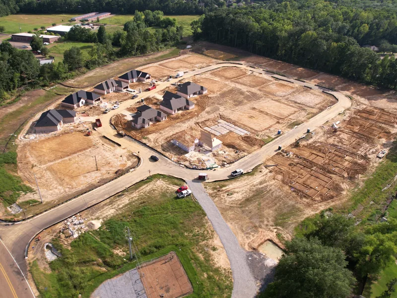 Angled drone photo of a residential subdivision with finished homes, framing, and foundations along a new street.